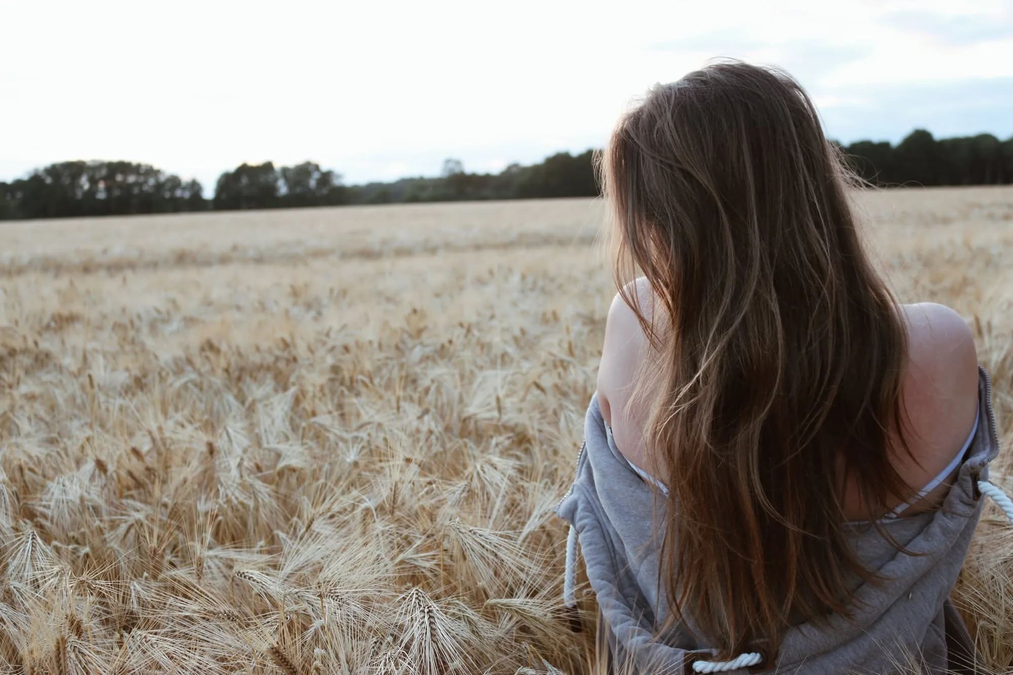 Portrait im Kornfeld: Frau mit langen braunen Haaren, von hinten fotografiert